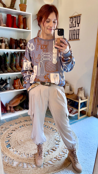 Soft and stylish light grey sweatshirt featuring a bold tackroom graphic pattern in copper and white modeled by Broker Leather Employee, Brooke.