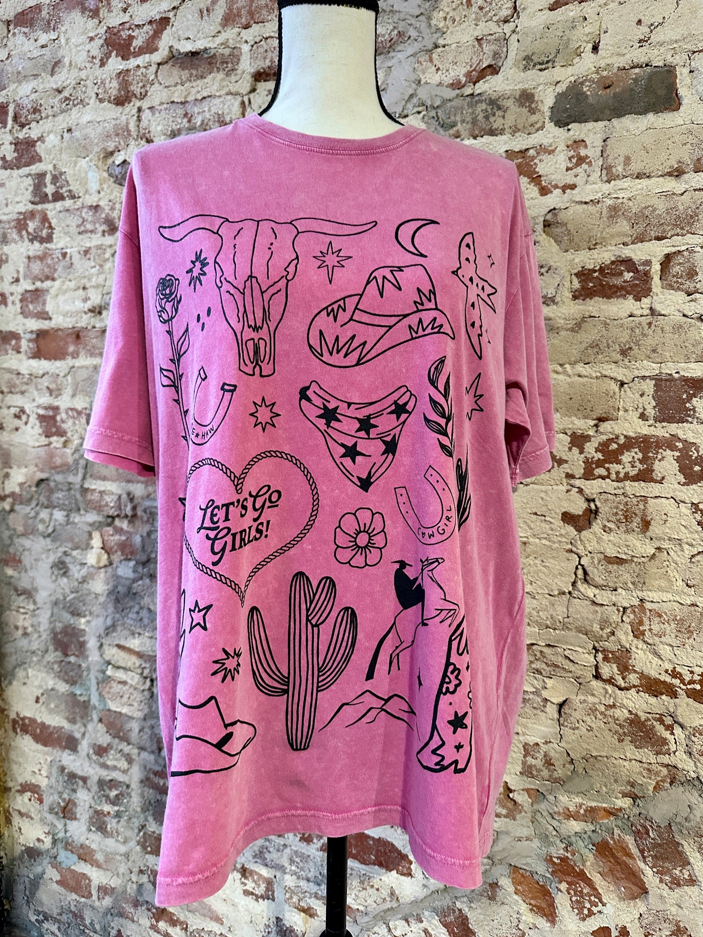 Broker Leather's Twain Cowgirl Mineral Washed Graphic Tee on a mannequin showing it's western icons such as the bull skull, cowboy hat, cactus, rose, horseshoes and rope heart.