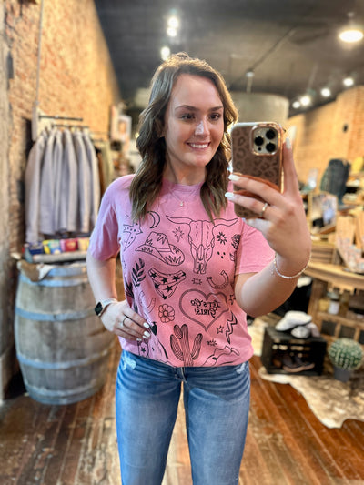 A model showing the western icons such as the bull skull, cowboy hat, cactus, rose, horseshoes and rope heart on the soft pink graphic tee.