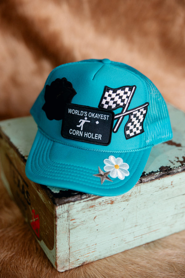 A photo of the World's Okayest Corn Holer Trucker Hat featuring a checkered flag, flower, star, and rose.